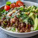 A close-up of a Low Carb Burrito Bowl with seasoned beef, sour cream, and fresh lime wedges ready to squeeze.