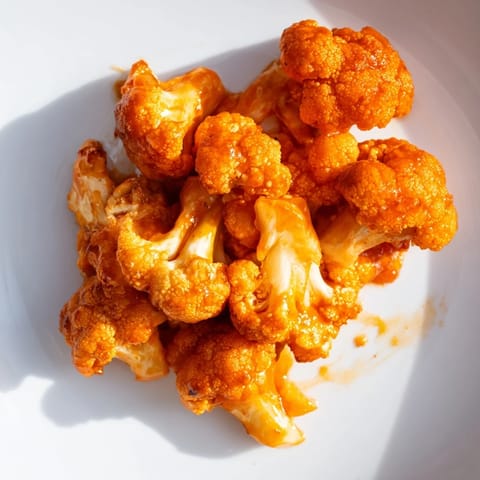 Golden, crispy battered cauliflower florets coated in tangy buffalo sauce, arranged on a baking sheet ready to be served.