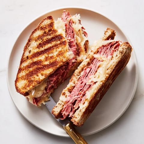A close-up of a Reuben sandwich, showcasing layers of corned beef and Russian dressing, served with potato chips and pickles.