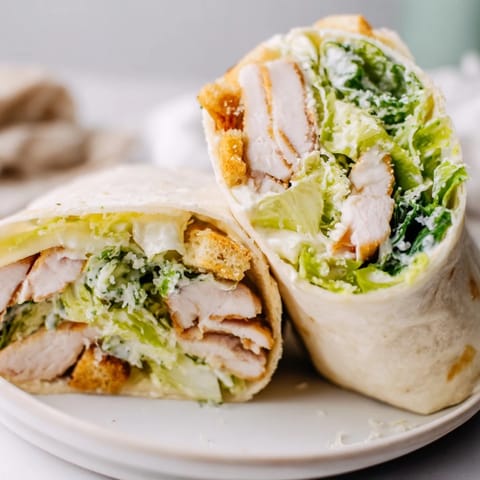 Sliced grilled chicken rests on romaine tossed in creamy Caesar dressing inside a soft flour tortilla.