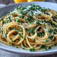 Vibrant lemon butter pasta with peas and Parmesan, topped with fresh parsley and a sprinkle of cheese.